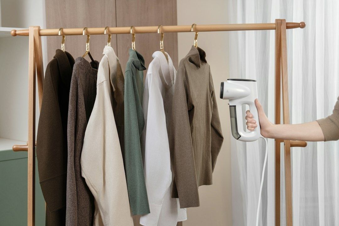 Handhållen steamer riktas mot kläder på en klädställning